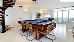 Une pièce spacieuse équipée d’une table de billard, d’un canapé et d’un escalier.