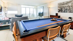 Une table de billard avec quatre chaises, un canapé, un téléviseur et un tableau représentant un paysage urbain.