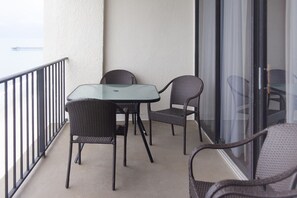 A balcony with a glass table and wicker chairs, a metal railing, and a view of the sea.