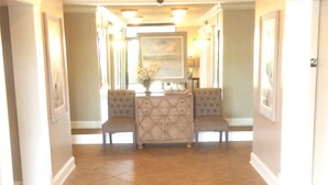 A hallway with a central seating area, flanked by framed pictures and a chandelier. - Oceanfront_Spacious_View the Sunrise_ Family Friendly & Quiet Building (Myrtle Beach)