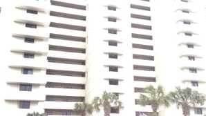 A high-rise building with multiple balconies and a parking area with cars. - Oceanfront_Spacious_View the Sunrise_ Family Friendly & Quiet Building (Myrtle Beach)