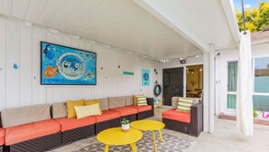 Um alpendre coberto com um sofá, duas mesas amarelas e uma pintura de peixes.