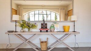 A wooden console table with a mirror above it, a window with curtains, and various decorative items including a vase with flowers, a yellow bucket, and a small basket. - Unique house with air con, wine country, pool 18x5, close Avignon (Cairanne)