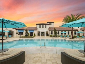 Un espace piscine avec des chaises longues et des parasols, un bâtiment doté d’un toit en tuiles et des palmiers.