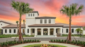 A two-story building with a white facade and a red-tiled roof, surrounded by palm trees and a landscaped garden.