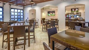 A spacious indoor dining area with multiple tables and chairs, ceiling fans, and large windows allowing natural light.