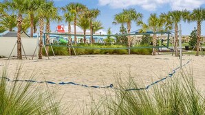 A beach volleyball court with palm trees and a clear sky.