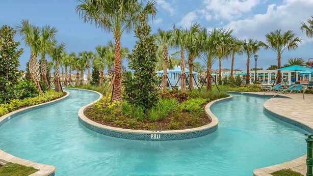 A swimming pool with a curved design, surrounded by palm trees and a tiled edge.