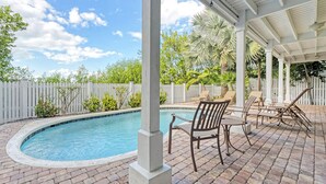 A covered outdoor swimming pool area with brick flooring, white columns, and lounge chairs. - Spacious Waterfront 4 Bedroom Home (Key West)