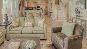A spacious living room with a sofa, armchairs, and a coffee table. A kitchen is visible in the background with wooden cabinets and modern appliances. - Spacious Waterfront 4 Bedroom Home (Key West)