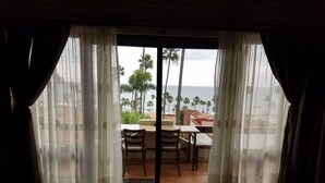 A room with a view of the beach and palm trees through sheer curtains.