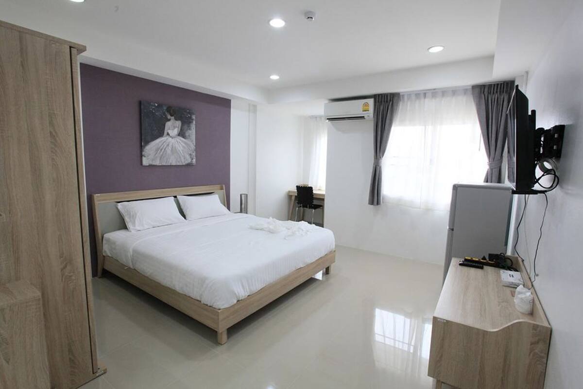 A modern hotel room with a wooden bed, a flat-screen TV, a desk, and a painting on the wall.