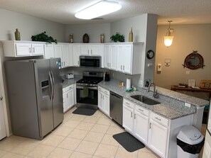 A modern kitchen with white cabinets, stainless steel appliances, granite countertops, and a small island with a sink.