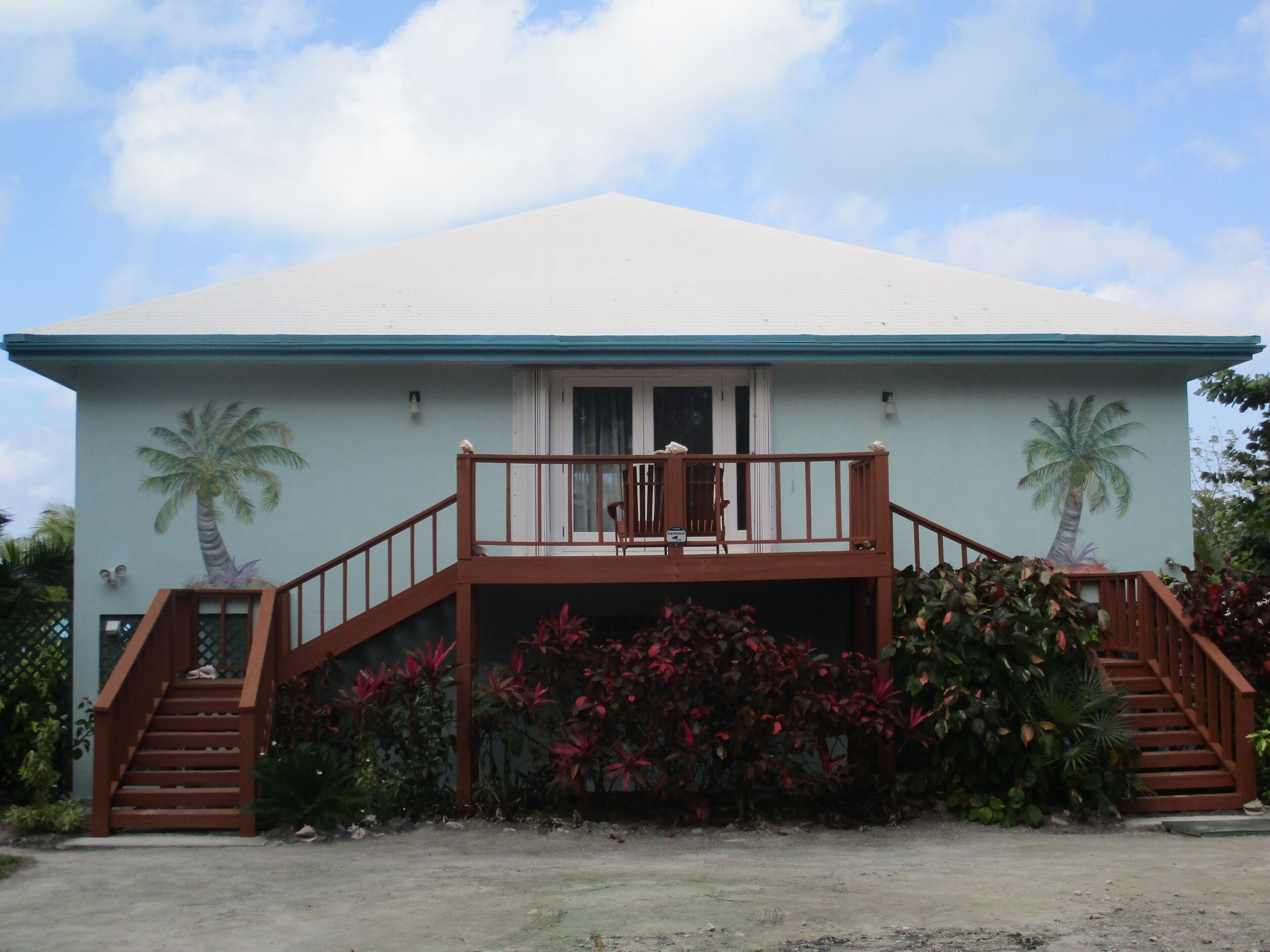 A two-story house with a balcony, palm trees painted on the walls, and a front porch with stairs.