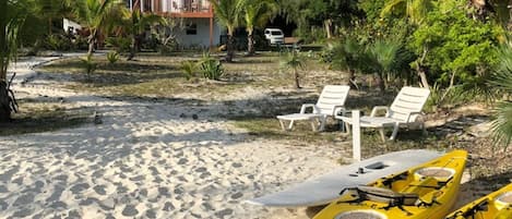 A beach with white lounge chairs, a white building, and yellow kayaks.