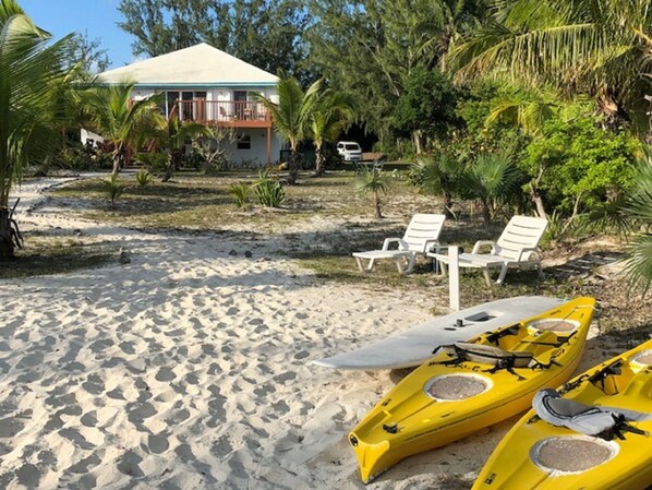 A beach with white lounge chairs, a white building, and yellow kayaks.