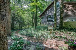 Un chalet rustique entouré d’une forêt dense, un chemin de briques menant à l’entrée et une enseigne en bois.