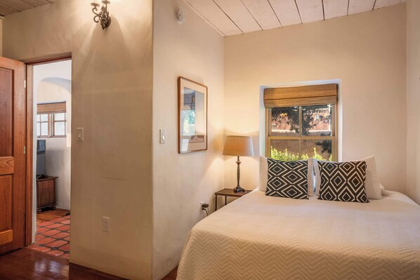Une chambre à coucher comprenant un lit, une table de chevet, une lampe, une fenêtre donnant sur un paysage agréable et une porte menant à une autre pièce.