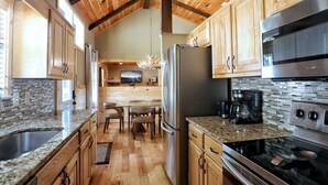Una cocina con armarios de madera, encimeras de granito, un refrigerador de acero inoxidable, una estufa y un comedor con mesa y sillas.