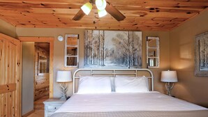 Un dormitorio con cama, techo de madera y una pintura de árboles.