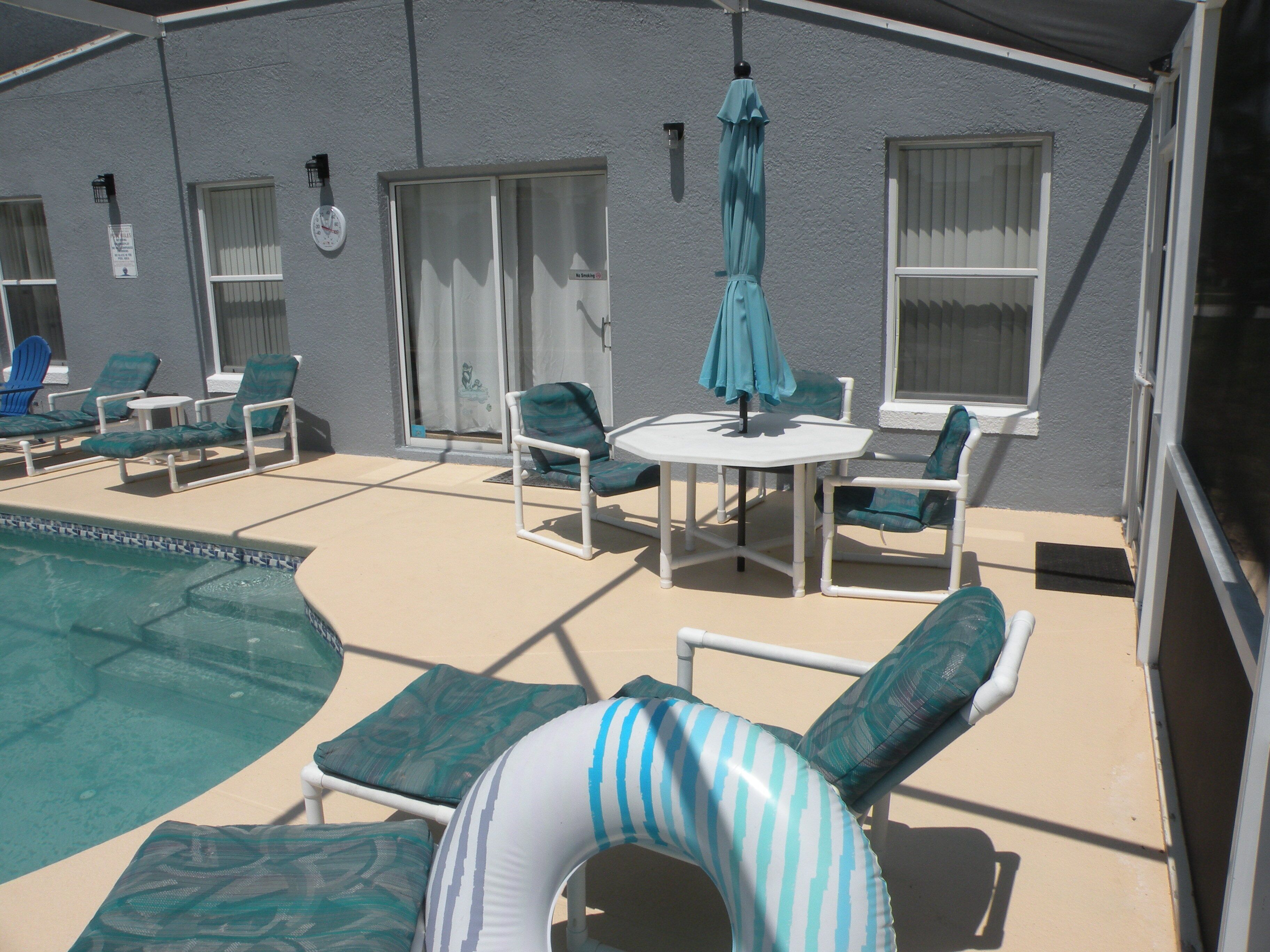 Área da piscina com espreguiçadeiras, uma mesa e um guarda-sol.