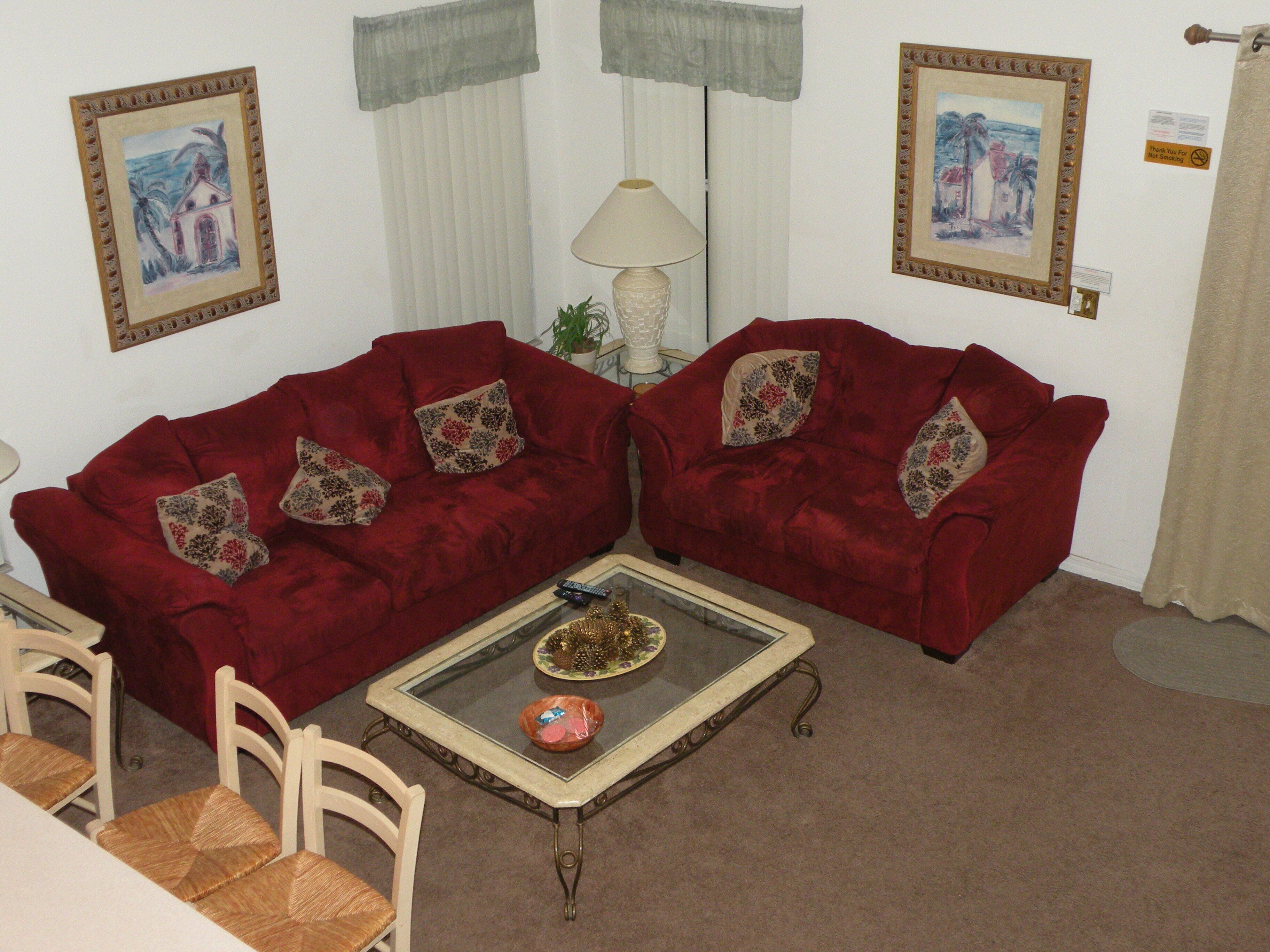 A living room with two red velvet sofas, a glass coffee table, and a white lamp.