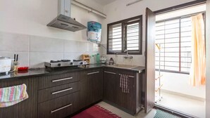 A kitchen with dark wooden cabinets, a gas stove, a range hood, and a window with blinds. - Ultra modern bungalow in Jakkur (Bengaluru)