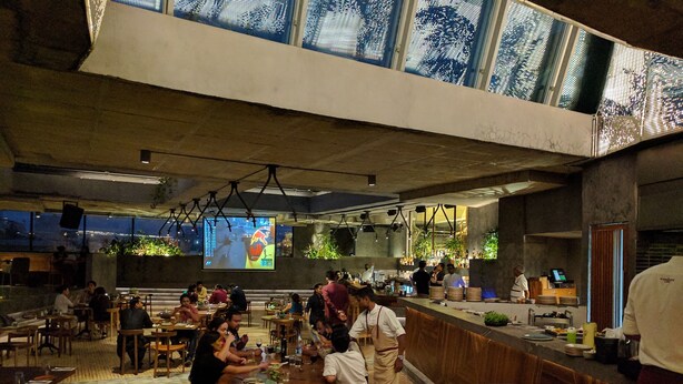 A restaurant with a high ceiling and large windows, featuring a bar area with staff and patrons. - Ultra modern bungalow in Jakkur (Bengaluru)