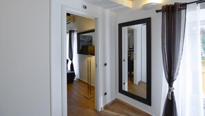 Un pasillo con un espejo, una puerta que da a una habitación y una ventana con cortinas.