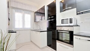 Una cucina moderna con mobili bianchi, forno integrato, microonde e una finestra con tende leggere.