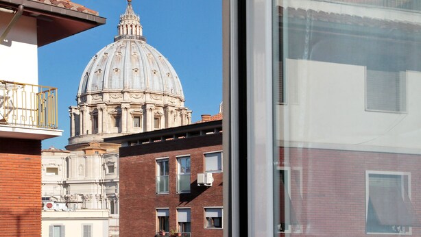 Vista di un edificio storico con una grande cupola e architettura classica, ripresa attraverso una finestra con un balcone.