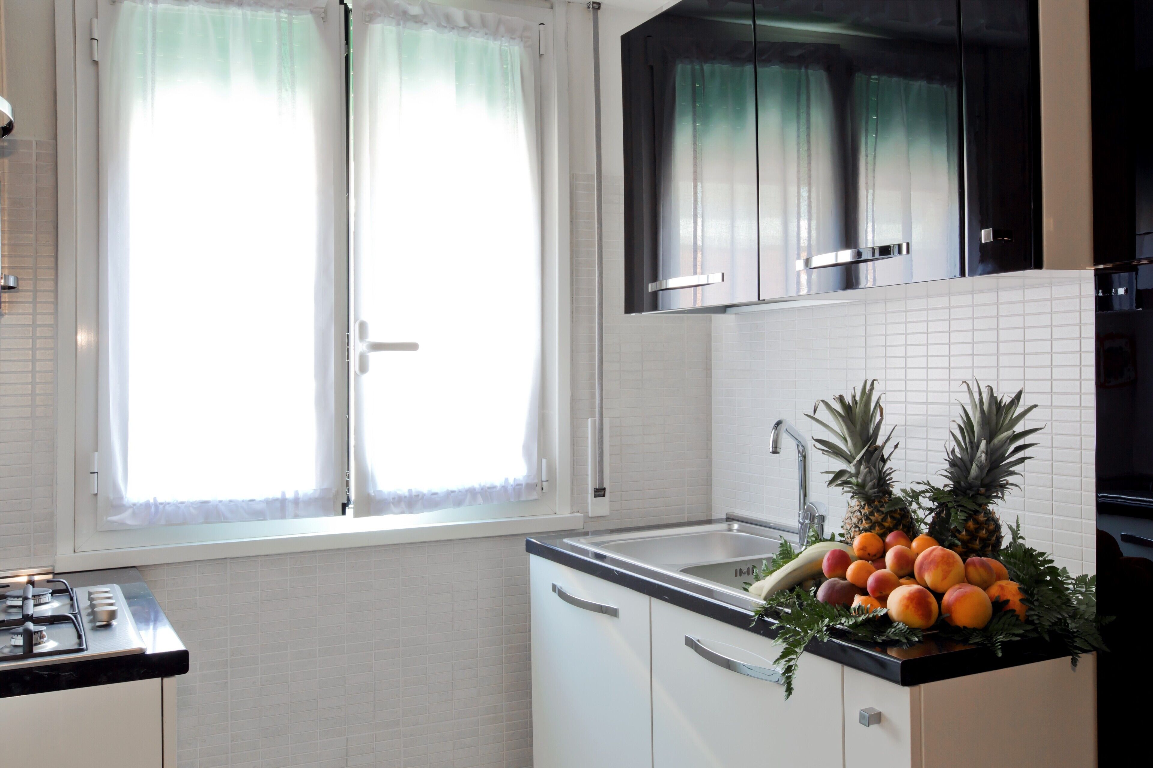 A kitchen with white cabinets, a black countertop, and a window with sheer curtains.