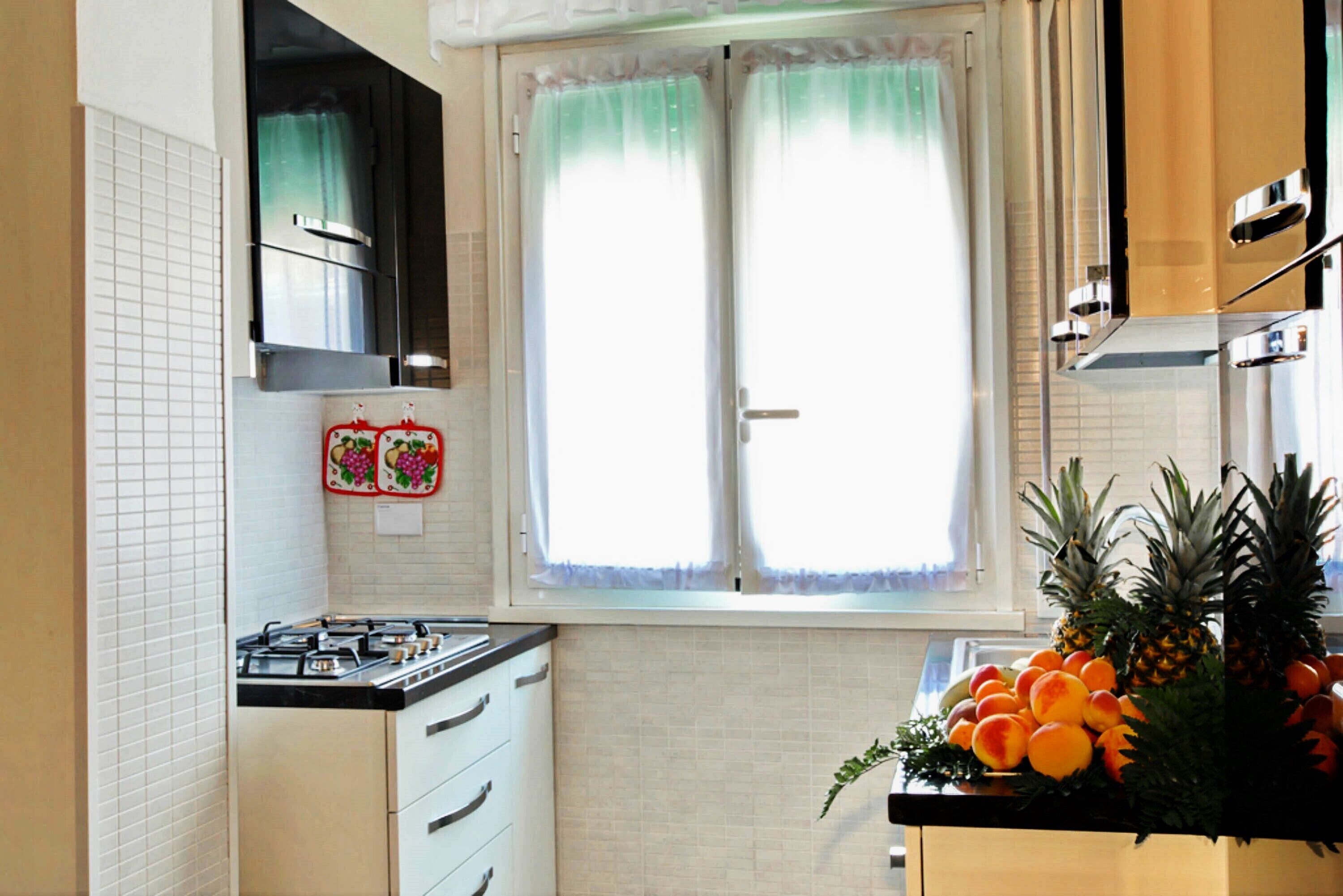 A kitchen with white cabinets, a stove, and a window with curtains.