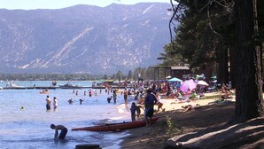 Une plage où l’on peut se baigner et faire du canoë, un quai avec des bateaux, et des montagnes en arrière-plan.