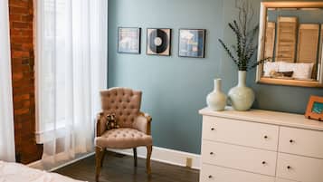 A bedroom with a tufted armchair, a dresser, and three framed items on the wall.