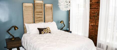 Un dormitorio con una cama grande, dos mesitas de noche, una lámpara de pared y una esfera blanca decorativa.