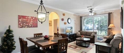A spacious living room with a fireplace, a dining area with a wooden table and chairs, and a large window with a view of the outdoors.