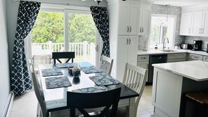 Une cuisine moderne avec des meubles blancs, un coin repas doté d’une table en verre et une vue sur un balcon.