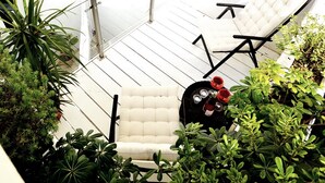 Una silla blanca acolchada con una bandeja de copas y botellas de vino tinto, rodeada de exuberantes plantas verdes.
