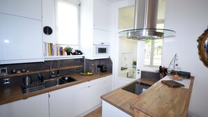 Una cocina moderna con gabinetes blancos, una campana extractora de acero inoxidable, un microondas integrado y una isla de madera con pileta.