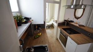 Una cocina moderna con horno empotrado, un lavamanos y una estufa. Hay una pequeña zona de comedor con una silla y una mesa.