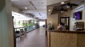 A hotel corridor with a reception desk, ceiling fans, and a view of the outdoor area with plants. - Charming Studio in Waikiki - 2 Full size Beds, Free Wi-Fi (Honolulu)