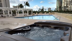 A hot tub with water jets, a pool, lounge chairs, and a pergola. - Charming Studio in Waikiki - 2 Full size Beds, Free Wi-Fi (Honolulu)