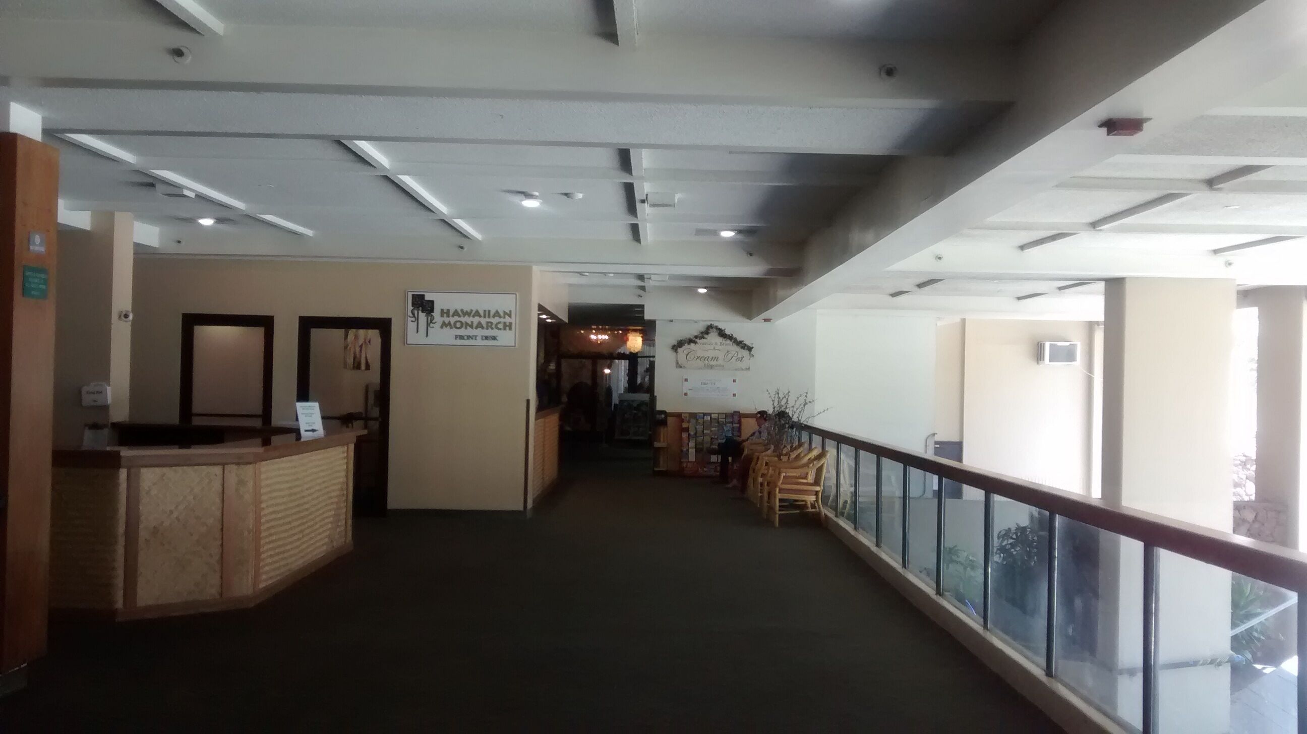Un hall d’hôtel avec un comptoir d’accueil, une enseigne indiquant « Réception Hawaiian Monarch » et une enseigne « Cream Pot ».