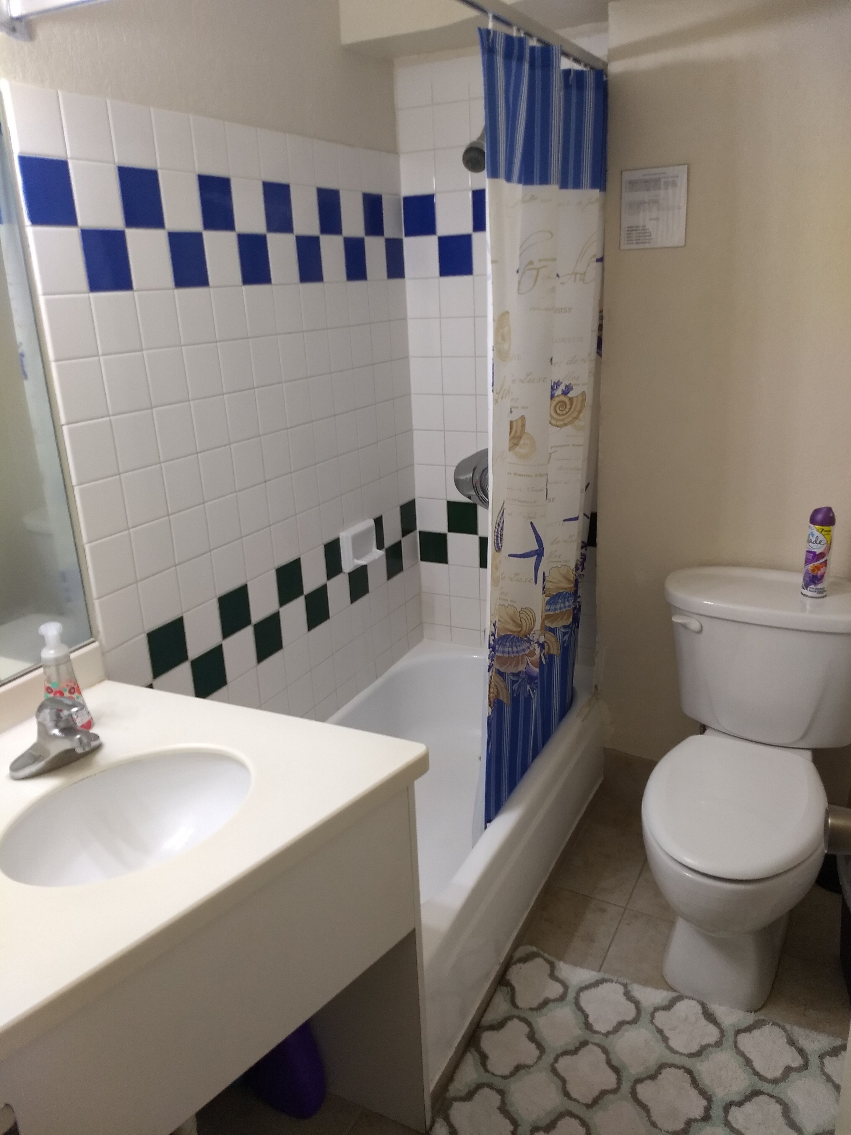 Et badeværelse med hvid vask, badekar med bruseforhæng, toilet og et mønstret gulv.