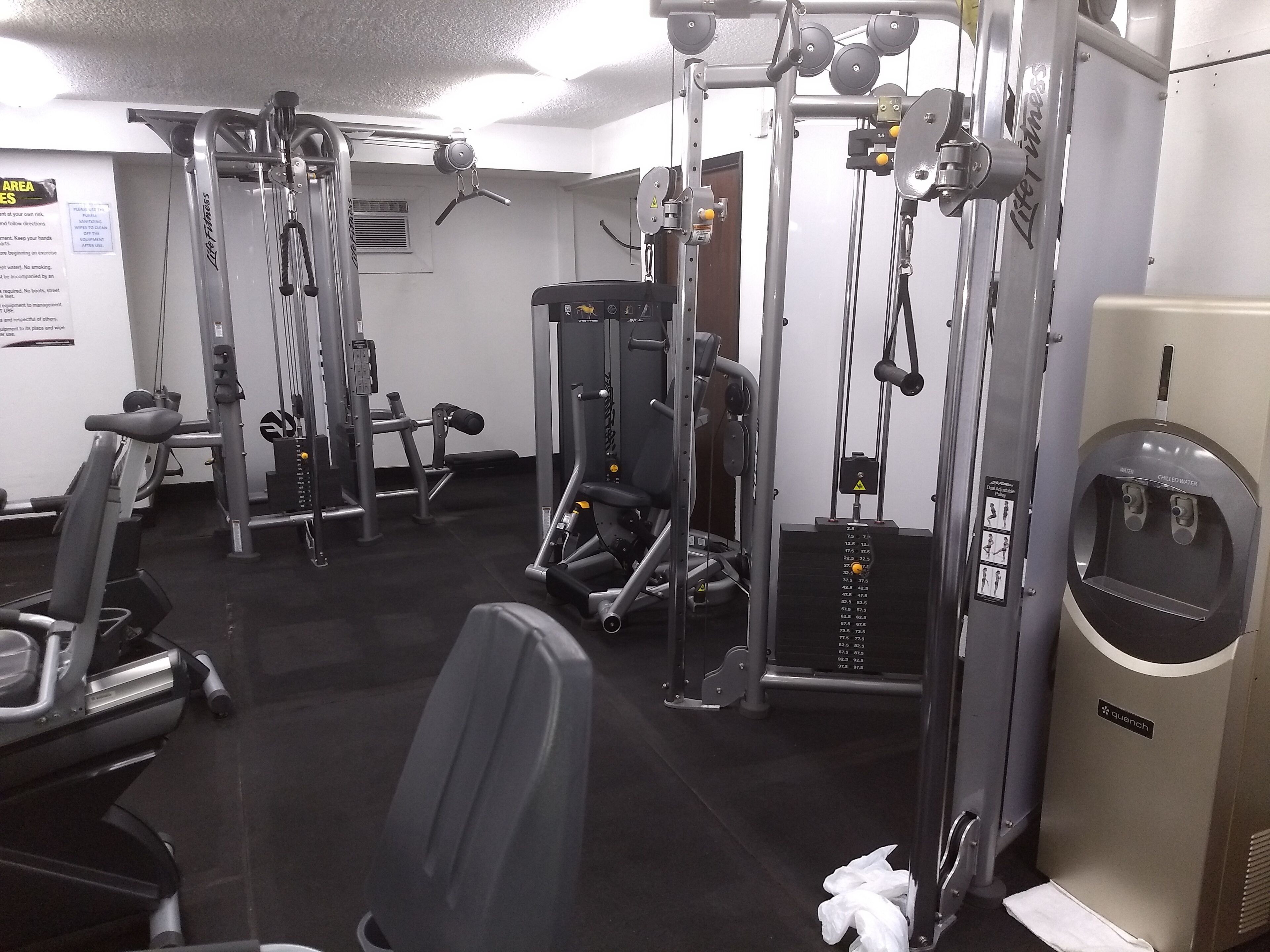 A gym with various exercise machines, a water dispenser, and a sign indicating the use of the facility.