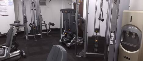 A gym with various exercise machines, a water dispenser, and a sign indicating the use of the facility.