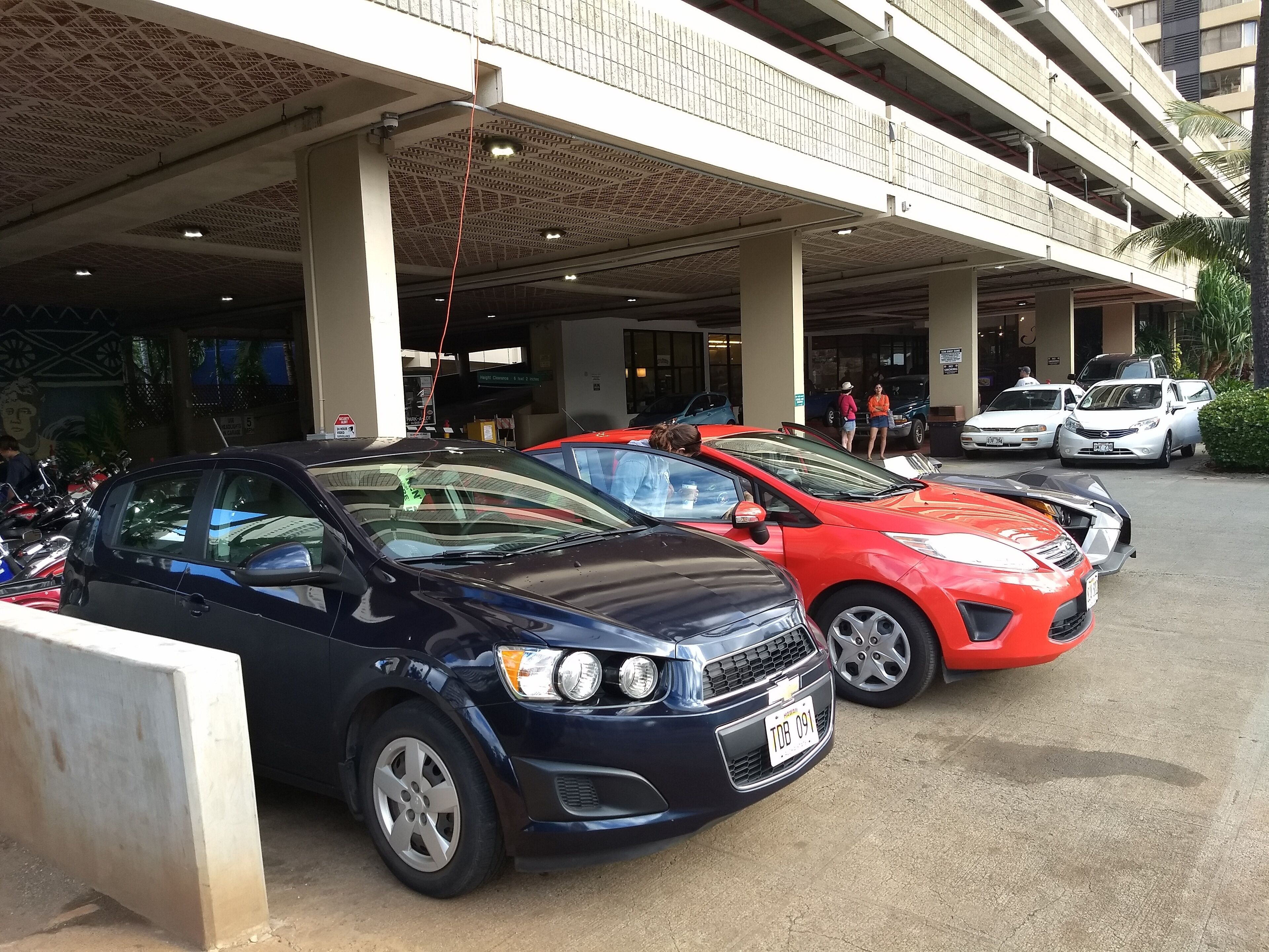 A parking area with multiple cars, a covered walkway, and a building entrance.
