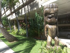 A tiki statue in a garden with palm trees and tropical plants, under a covered walkway. - Charming Studio in Waikiki - 2 Full size Beds, Free Wi-Fi (Honolulu)
