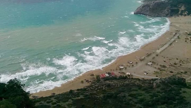Una playa costera con terreno rocoso y algunas construcciones cerca de la orilla.